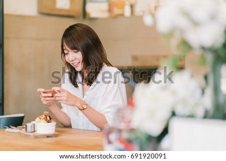 Beautiful Asian girl taking photo of sweet desserts at coffee shop, using smartphone camera, posting on social media. Food photograph hobby casual relax lifestyle, modern social network habit concept