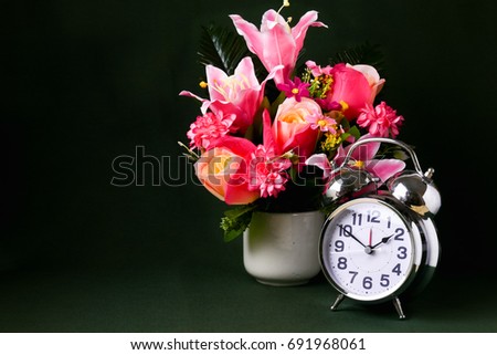 A silver alarm clock and a vase of pseudo pink lily and rose flower, still life