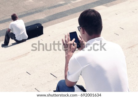 Young man with mobile phone and man with suitcase, shallow depth of field, toned photo