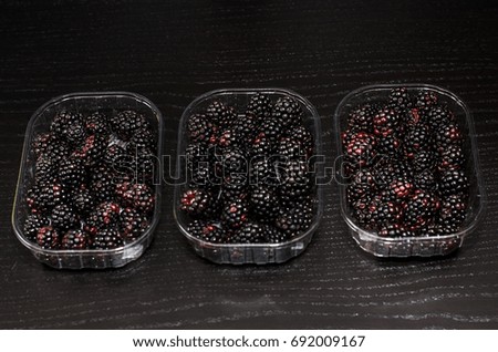 3 boxes of fresh blackberries on a black wooden background