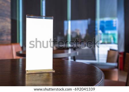 Mock up Menu frame in Bar restaurant ,Stand for booklets with white sheets of paper acrylic tent card on wooden table on cafeteria blurred background