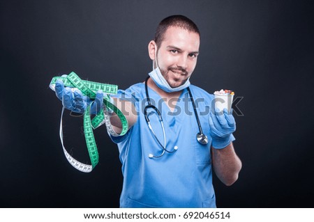 Plastic surgeon wearing scrubs holding measuring tape first and pills smiling on black background