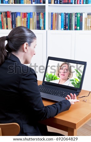 Rear view of a business woman in her office in front of her laptop, having a video call with her physician by means of the internet, telemedicine or telehealth concept