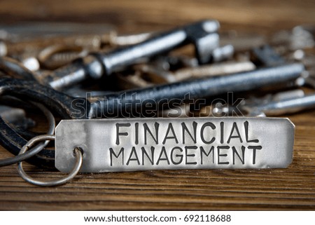 Photo of key bunch on wooden board and tag with letters imprinted on clean metal surface; concept of FINANCIAL MANAGEMENT