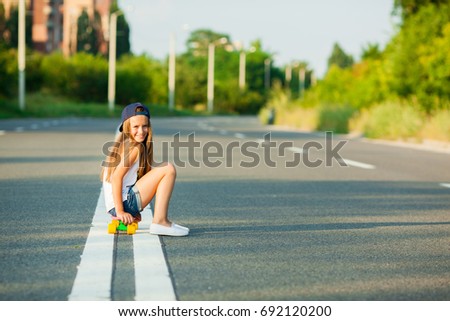 A young girl with penny board outside the city at the road. 
