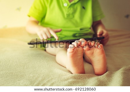 Kid with tablet sitting on bed and watching cartoons. Focus on the feet