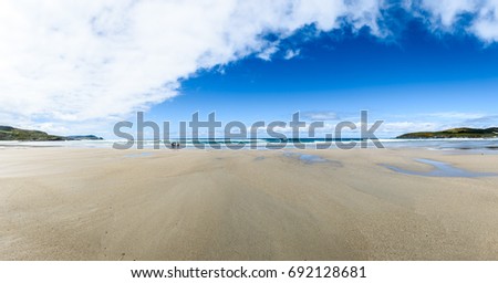 Mother and children are walking on sandy Atlantic beach. Family walking on a beach on vacations in warm clothes. Panoramic landscape picture.