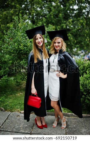 Two amazing young female graduates standing outside in graduation gowns and caps.