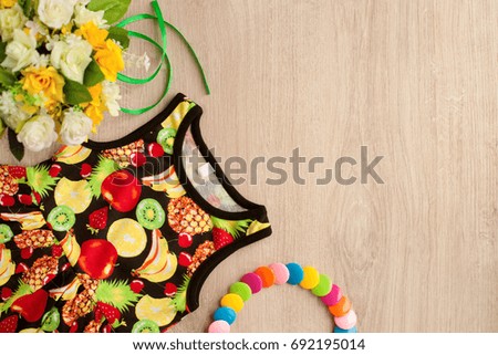 Summer dress for a girl. Dress in a tropical style and bright beads. View from above. Summer dress with a picture of tropical fruits. Clothes for the girl on the table. Summer clothes for children.