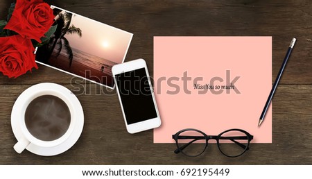 Two red roses on the old lovely photo and Miss you so much written on pink paper with eyeglasses pencil and hot coffee on wooden background.