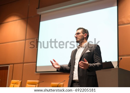 Speaker giving talk on podium at Business Conference. Entrepreneurship club. Copy space on white screen. Royalty-Free Stock Photo #692205181