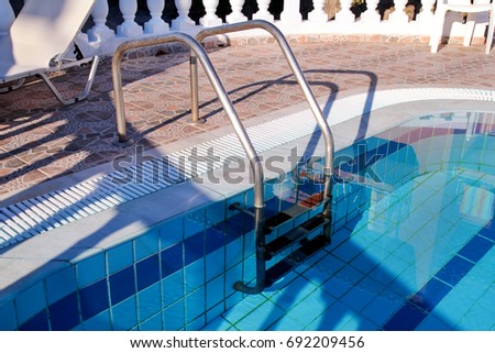 Handrail on the pool. Pool handrails view. Water swimming pool with stair with sunny reflections, closeup. Steel handrail, swimming, summer, travel. The entry to the pool with handrail.