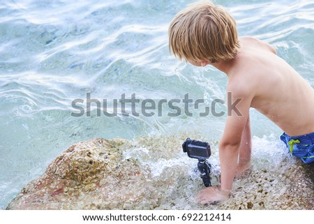 Child boy shooting movie with action outdoor waterproof camera in the sea