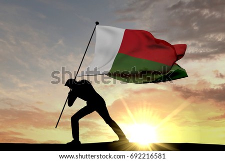 Madagascar flag being pushed into the ground by a male silhouette. 3D Rendering
