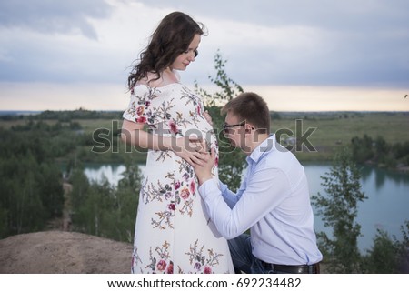A man is hugging a belly of a pregnant woman against a lake