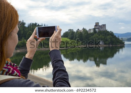 girl taking a picture of a beautiful castle on a lake shore with her smartphone
