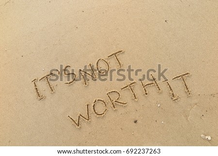 Handwriting  words "IT'S NOT WORTH IT" on sand of beach. Royalty-Free Stock Photo #692237263