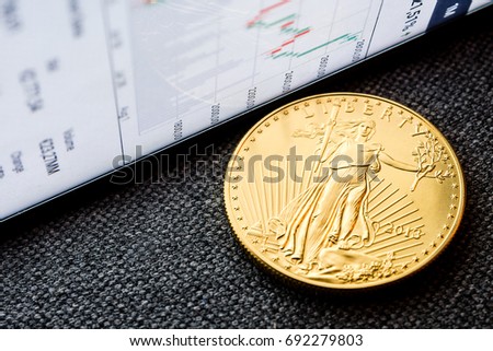 closeup of golden american eagle coin with a chart reflection on close digital device with green and red bars