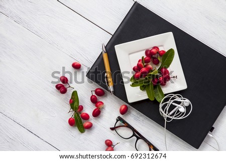 A notebook and red fruit on white wooden table and soft light background, work space concept.