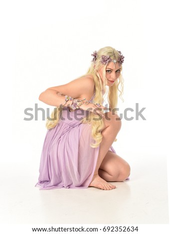 Full length portrait of a pretty blonde girl  wearing a purple fairy dress. seated pose, isolated against white background.