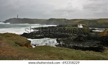 Giant Waves Nature Show crashing against dark colored cliffs, lighthouse h of Meirás, and church of Virgen of the Port, A coruna, Galicia, Spain, raising a white foam dozens of meters against sky 