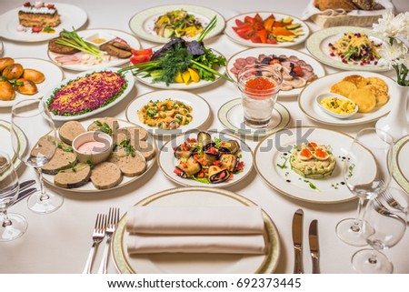 Restaurant table, many different dishes. Plates, forks, knives, glasses on a white tablecloth. Delicious healthy fresh food. Royalty-Free Stock Photo #692373445