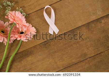 Close-up of pink Breast Cancer Awareness ribbon by gerbera flowers on wooden table