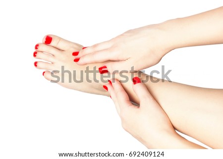 Woman with beautiful red manicured nails displaying her bare feet with her hands on her ankles on white. Fashion concept.