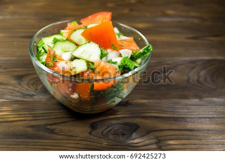Fresh salad with tomato, cucumber, onion, parsley and dill in glass bowl on wooden table