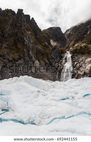 A waterfall on the side of a mountain with a glacier in the foreground. 