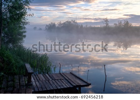 Early morning on a wooden boat pier of misty river Royalty-Free Stock Photo #692456218