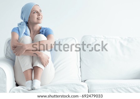Joyful breast cancer survivor holding her knees while relaxing on a couch