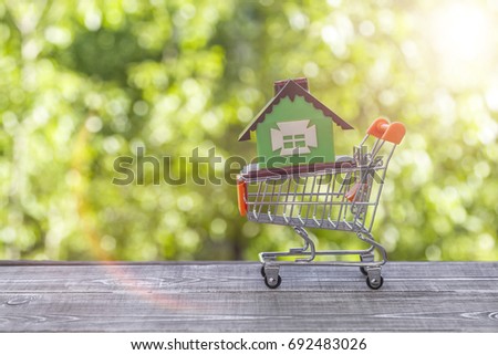 Concept eco house in a shopping cart on a background of greenery. Idea: buying a house, renting out, selling real estate. Mortgage. Loan for housing.