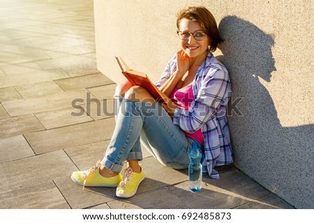 Smiling adult female drinking water and reading a book. Recreation in the city and health