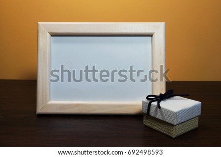 Blank photo wooden frame with gift box on the table.