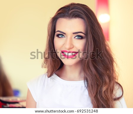 Portrait of young attractive woman with a stylish makeup smiling in front of the makeup mirror