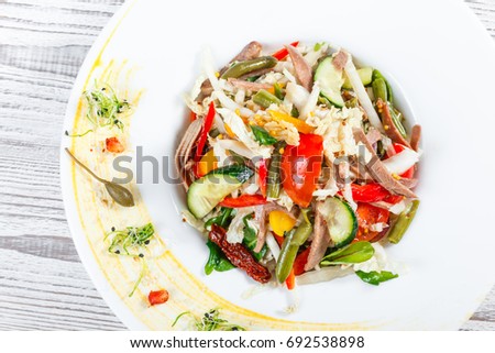 Fresh vegetable salad with cow tongue, spinach, green beans, tomatoes, sweet peppers, cabbage, mustard and dried tomatoes on plate on light wooden background. Healthy food. Top view
