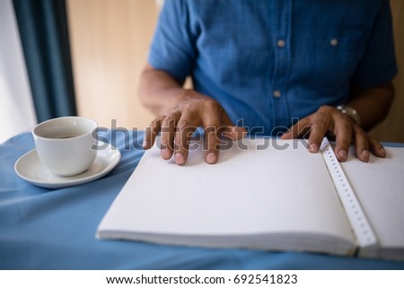 Midsection of senior man reading book by coffee cup at table in retirement home