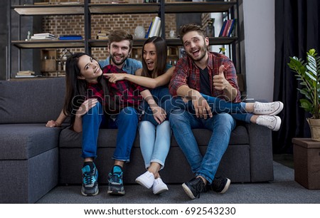 A company of happy young friends are resting and fooling around at home on the couch