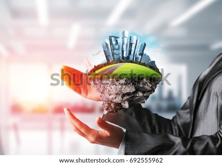 Cropped image of business woman in suit keeping green island with metropolis city in her hands. Mixed media. Office view with sunlight on background.