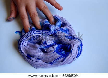 New picture of Child's hand playing with lilac slime, with blue food coloring added to it. this is a home made slime, made with borax, glue and glitter. 