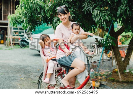 Family portrait of Asian people : 4 months baby and 3 years kid riding on bicycle feeling happy and smile with her mother in the garden.
