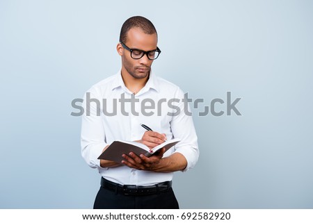 Education, work and success concept. Nerdy academic african professor is thoughtful, in glasses, holding a notebook and writes information Royalty-Free Stock Photo #692582920