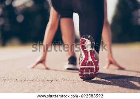Ready to go! Close up cropped low angle photo of shoe of female athlete on the starting line of a stadium track, preparing for a run. Sunny spring day Royalty-Free Stock Photo #692583592