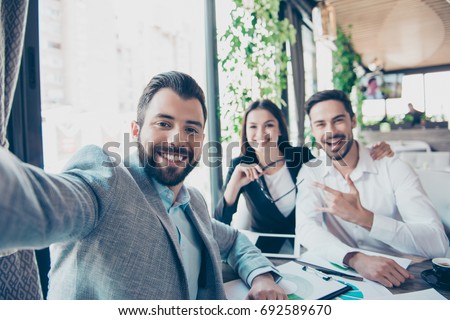 Happy friends business partners are making selfie photo, sitting in the terrace of the restaurant. They are posing, smiling and gesturing, all wearing formal smart outfits Royalty-Free Stock Photo #692589670
