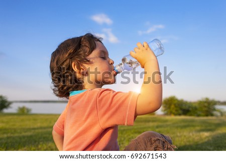A child drinks water from a bottle while walking, baby health. Royalty-Free Stock Photo #692671543