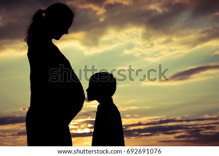 Mother and son walking on the field at the sunset time. People having fun outdoors. Concept of friendly family.