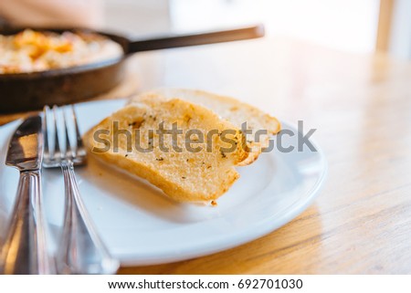 The close up of the garlic bread on the white dish on the wooden table.