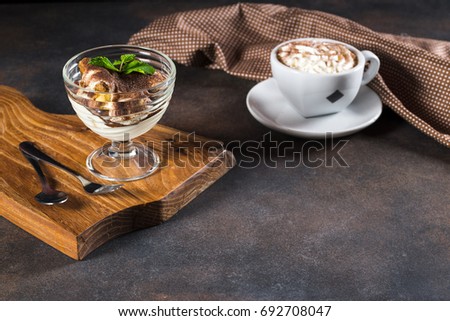 Tiramisu, traditional Italian dessert in glass on a wood plate and grey stone background. Coffee and milk cream.