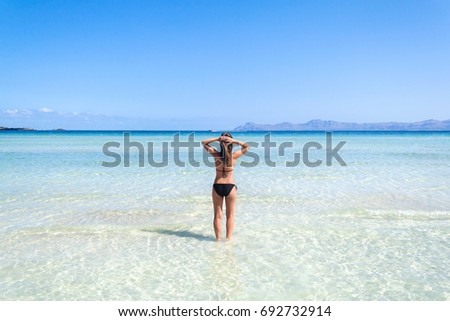 Young woman in bikini standing in clear blue water on the beautiful beach of Alcudia, Mallorca, Spain.